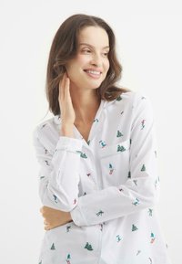 Biała koszula z guzikami, zdobiona kolorowym wzorem na temat narciarstwa, z narciarzami i drzewami; gładki materiał z długimi rękawami i kołnierzykiem.