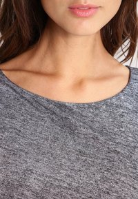 Tessuto grigio e strutturato con un ampio scollo, che presenta un aspetto liscio e morbido. Dettaglio della zona del petto e della clavicola.