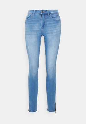 Jeans skinny em denim azul claro com um acabamento desgastado, apresentando um detalhe em zíper no tornozelo e um design tradicional de cinco bolsos.