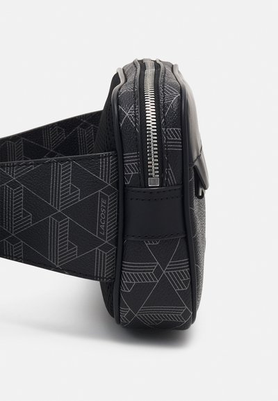 Sac noir avec des motifs géométriques, accents en cuir, forme plate et fermeture éclair sur le côté. Équipé d'une sangle texturée et d'un détail de marque.