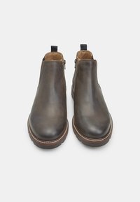 Stivali alla caviglia in pelle marrone con una finitura liscia, punta rotonda, cerniere laterali e cuciture decorative lungo la suola.