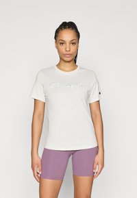 Ανοιχτό γκρι βαμβακερό t-shirt με το λογότυπο "Champion" σε καλλιγραφικό κείμενο, συνδυασμένο με μωβ αθλητικά σορτς. Κοντά μανίκια, λαιμός σε στρογγυλό σχέδιο.