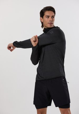 Zwart trainingshemd met lange mouwen en een gestructureerde afwerking, met een half-rits kraag en oranje accenten, gecombineerd met zwarte shorts.