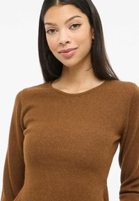 Pruun soonikkoe Hõlmikuga pikkade varrukatega t-särk ümar kaelusega. Kangas tundub pehme ja tekstureeritud, horisontaalse soonikkirjaga üle kogu pinna.