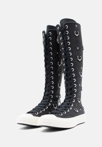 Botas de tecido até ao joelho, pretas, com ilhoses prateados e acentos circulares. Apresenta um bico em borracha branca e um design de atacadores texturizado.