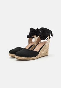 Svarte lerret kile espadriller med flettet jute-hæl og stoff ankelseler med volanger, åpne sider og flat såle.