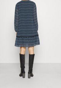 Kleid mit Marine-Navy-Muster, langen Ärmeln und stufigem Saum, kombiniert mit schwarzen kniehohen Stiefeln mit Absatz und strukturierten Absätzen.