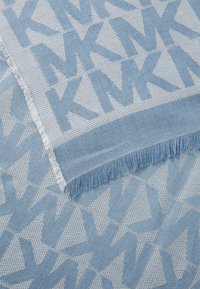 Tissu tissé bleu clair présentant un motif géométrique répétitif avec de grandes lettres "KM". Les bords sont finis avec des détails effilochés.