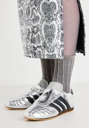 Sølvfodboldstøvler med sorte striber og et strømlinet design, parret med strukturerede grå og guld stribede sokker og et mønstret nederdel.