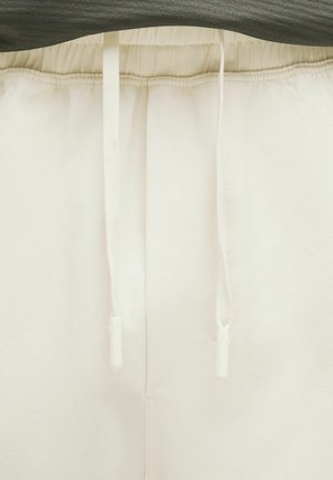 Pantaloni della tuta bianchi con cintura elastica e laccetto, caratterizzati da una texture liscia e linee pulite. Nessun motivo o dettaglio visibile.