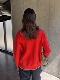 Piros kötött pulóver laza szabással, bordás aljúval és hosszú ujjal. Fekete csíkos nadrággal és puha barna táskával párosítva.