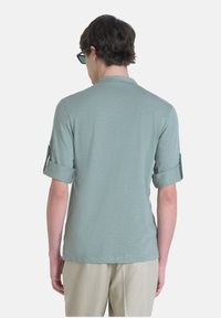 Camicia verde chiaro a maniche corte con risvolti, realizzata in materiale morbido, caratterizzata da un design semplice e da un collo a giro.