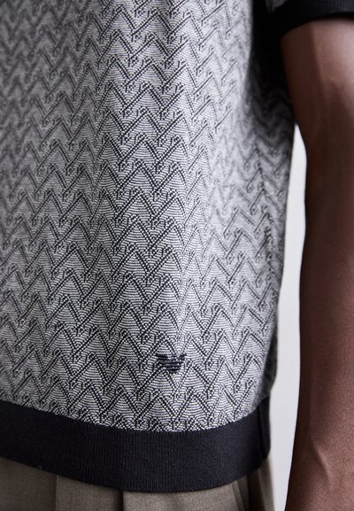 Pull en tricot noir et blanc présentant un motif géométrique avec un ourlet côtelé noir contrastant. Détail de logo subtil près de l'ourlet.