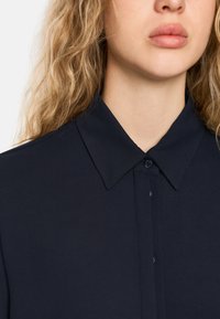 Navy blue collared shirt featuring a button-up front, smooth texture, and neatly stitched edges. Classic design with a structured collar.
