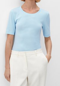 Ljusblå kortärmad t-shirt med rund halsringning, ihop med högmidjade vita byxor, som har en slät textur och en figurnära silhuett.