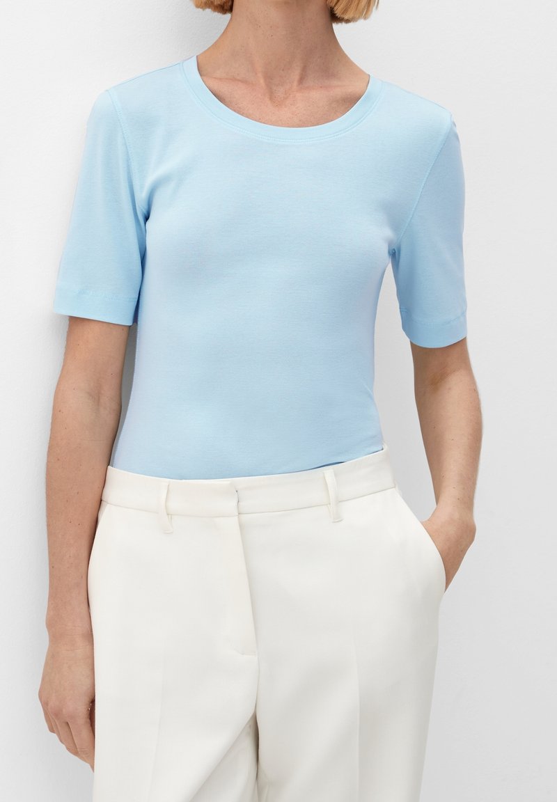 Ljusblå kortärmad t-shirt med rund halsringning, ihop med högmidjade vita byxor, som har en slät textur och en figurnära silhuett.