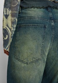 Světle modré džíny z denimu s vybledlou texturou, vybavené zadní kapsou a kontrastním prošíváním. Design má uvolněný st řih.