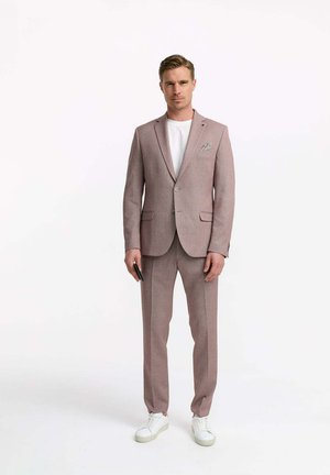 Light pink suit jacket and pants made of textured fabric, paired with a white t-shirt and white sneakers. Pocket square visible in the jacket.