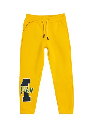 Pantalones de chándal amarillos con cintura elástica, cordón, dos bolsillos laterales y un diseño de logo en negro y verde en el muslo izquierdo.