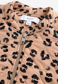 Quiltet jakke i beige med sort leopardmønster. Har en frontlynlås og et mærke. Materialet ser blødt ud med en struktureret overflade.