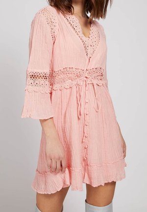 Robe rose texturée avec des manches cloche et des accents en dentelle. Présente un décolleté en V, une fermeture à boutons et un nœud à la taille. Ourlet froncé.