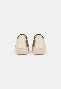 Baskets dorées métalliques à finition lisse, avec des accents noirs contrastants au talon et des semelles en caoutchouc beige texturé.