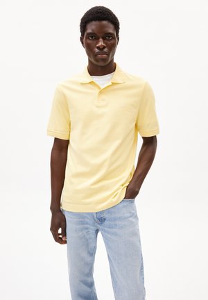 Gelbes Polohemd mit kurzen Ärmeln und einem kleinen Logo auf der Brust, kombiniert mit hellblauen Jeans. Glatte Textur, klassisches Design.