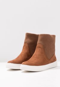 Brązowe zamszowe botki za kostkę z prążkowanymi, dzianinowymi cholewkami, białymi gumowymi podeszwami i gładką fakturą; elegancki, nowoczesny design z minimalną ilością szwów.