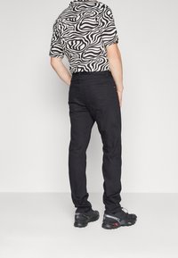 Pantalones de mezcla de algodón negros combinados con una camisa de manga corta de patrón de cebra en blanco y negro y zapatillas deportivas negras.