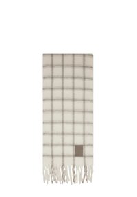Coperta a quadri intrecciati in crema e grigio, con bordi frangiati e un patch logo argento nella parte inferiore. Texture morbida e forma rettangolare.