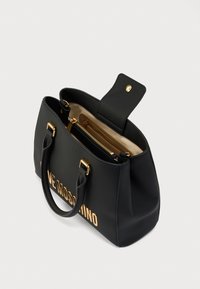 Μαύρη υφασμάτινη τσάντα με υφή, με χρυσά γράμματα, διπλές λαβές και θήκη με φερμουάρ, με κούμπωμα στην κορυφή.