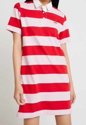 Femme portant une robe polo à manches courtes rayée horizontalement rouge et rose clair, avec un col blanc et deux boutons.