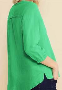 Grön, lätt blus med trekvartslånga ärmar, rundad fåll, veckdetalj bak och en mjuk, strukturerad yta.