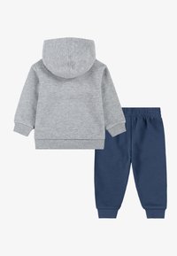 Siva kapuca s puloverjem z ribastimi manšeti, v kombinaciji z mornarskimi modrimi hlačami za prosti čas, ki imajo elastičen pas. Obe izdelani iz mehkega materiala.