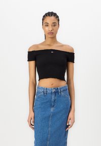 Top nero off-the-shoulder in tessuto strutturato e smock, abbinato a una gonna in denim blu a vita alta, con chiusura a bottoni frontale.