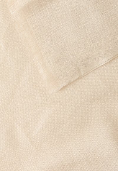 Gros plan d'un tissu beige doux avec un bord plié montrant une fine texture tissée et des détails subtilement effilochés.