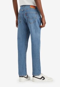 Vaaleansiniset farkut rentolla istuvuudella, joissa on kaksi takataskua ja nahkainen merkintä vyötäröllä. Valkoiset lenkkarit, joissa mustat yksityiskohdat.