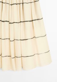 Un tissu crème présente des rayures foncées horizontales, mettant en valeur la texture et le tombé d'une jupe froncée.