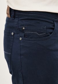 Navy blue pants with subtle texture, featuring a small front pocket, contrasting stitching, and a leather patch on the waistband.
