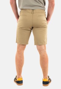 Pantalones cortos caquis con un diseño ajustado, dos bolsillos traseros y una textura de algodón suave. Combinados con zapatillas azul y amarillo.