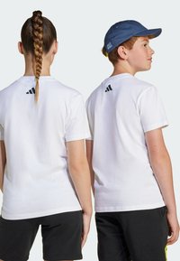 White cotton t-shirts with crew neck, short sleeves, and black Adidas logo on the back. Equipped with black shorts, displaying a casual look.