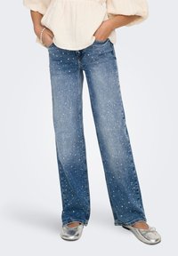 Šviesiai mėlynos spalvos džinsai tiesaus kirpimo, papuošti išsklaidytomis akutėmis. Derinami su plokščiais sidabriniais batais.