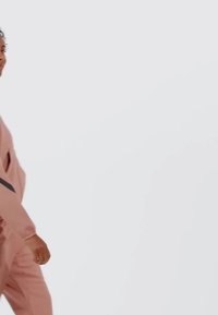 Chándal rosa claro de corte relajado, con una franja diagonal negra en la chaqueta. Textura suave, costuras visibles y puños elásticos.