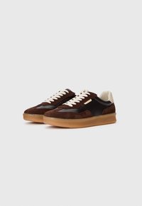Sneakers din suede maro cu un panou din piele neagră, șireturi crem și o talpă din cauciuc de tip gumă, cu un design texturat.