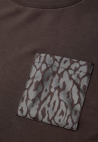 Braunes T-Shirt mit glatter Textur und einer grauen Tasche mit Leopardenmuster. Einfacher runder Ausschnitt, leichter Glanz auf dem Taschentuchstoff.
