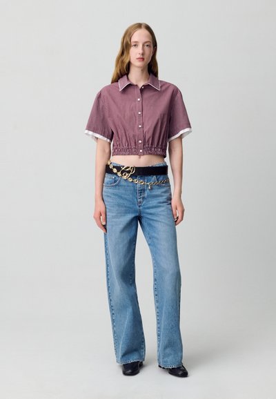 Camisa recortada de cuadros vichy rojos y blancos con mangas cortas y ribete blanco; combinada con jeans azules claros acampanados y un cinturón negro con detalles dorados.