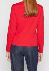 Rode katoenen top met lange mouwen en een ronde hals, aansluitend ontwerp en een rechte zoom, gecombineerd met donkerdenim jeans met achterzakken.