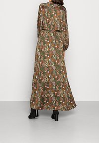Maxi-jurk in een groen bloemenpatroon met lange mouwen, een geplooid taille en een vloeiende rok. Gemaakt van lichtgewicht stof met een subtiele glans.