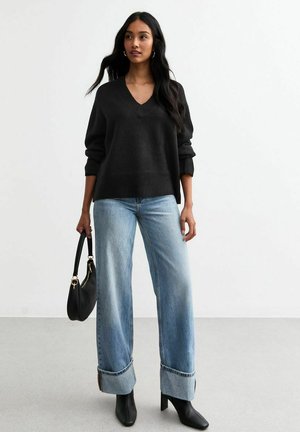 Pull noir à col en V, coupe décontractée ; jeans larges bleu clair avec ourlets retroussés ; bottines à talons noires ; portant un sac à main noir.