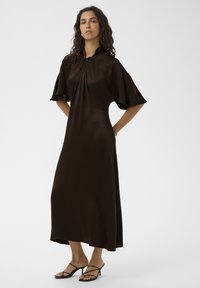Robe midi marron avec manches courtes, détail plissé à l'avant et coupe décontractée ; fabriquée dans un tissu lisse et fluide. Talons noirs à brides.